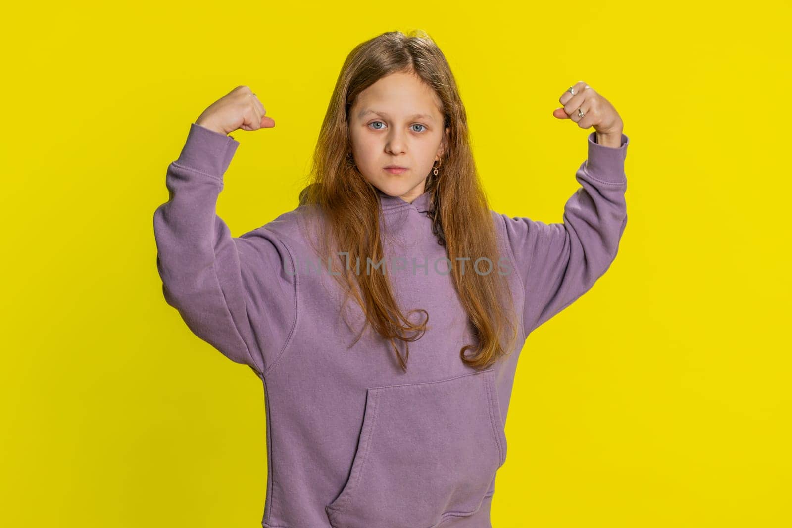 I am strong and healthy. Young cute girl showing biceps and looking confident feeling power strength to fight for rights, energy to gain success win. Preteen redhead child kid on yellow background