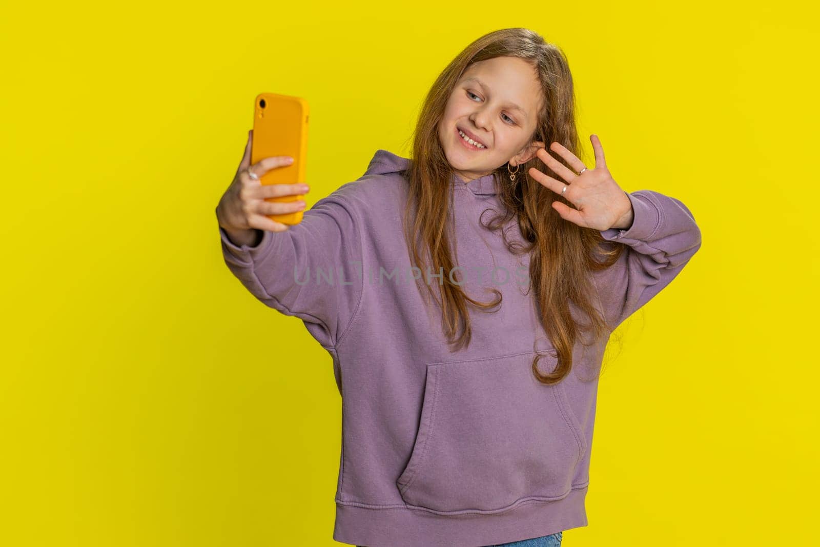Happy preteen child girl kid blogger taking portrait selfie on smartphone, communicating record video call online with social media subscribers. Teenager little children isolated on yellow background