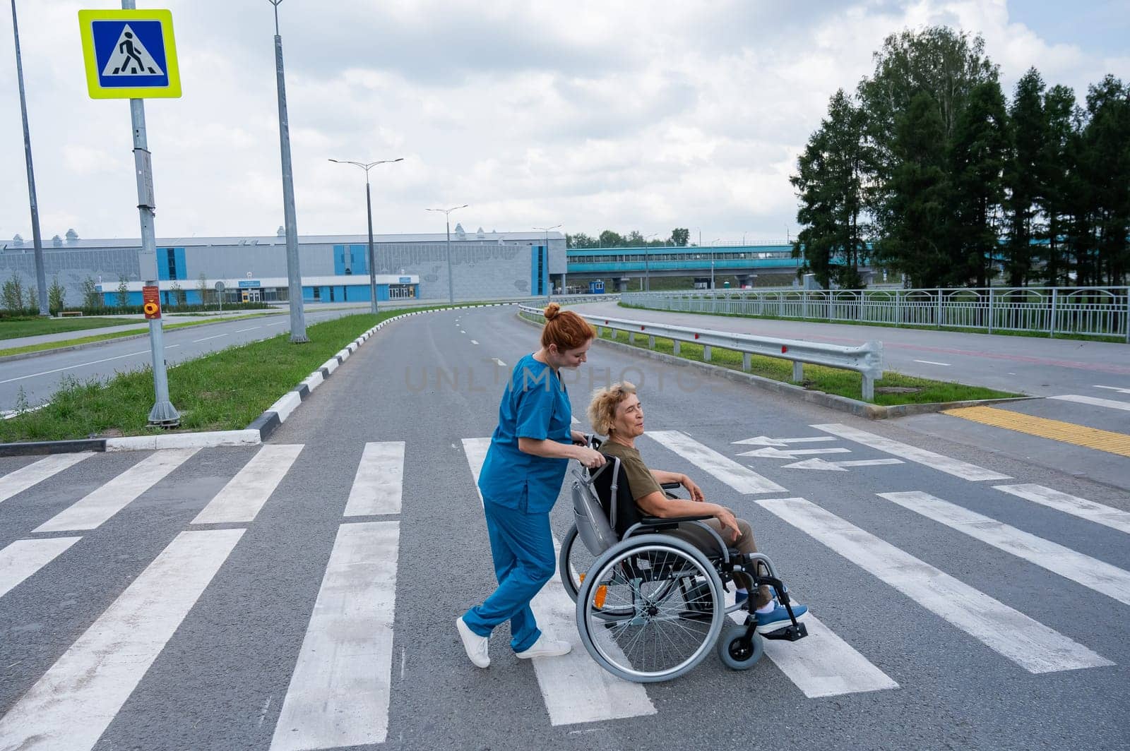 Profile of a nurse helping an elderly woman in a wheelchair cross the road. by mrwed54