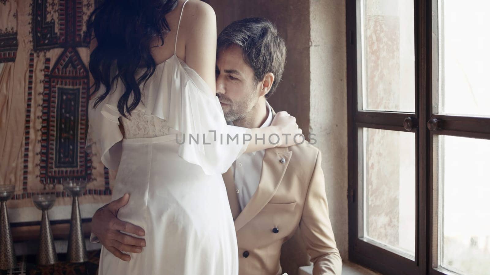 Just married couple embracing during photosession. Action. Happy bride and groom in wedding dress in beige room interior