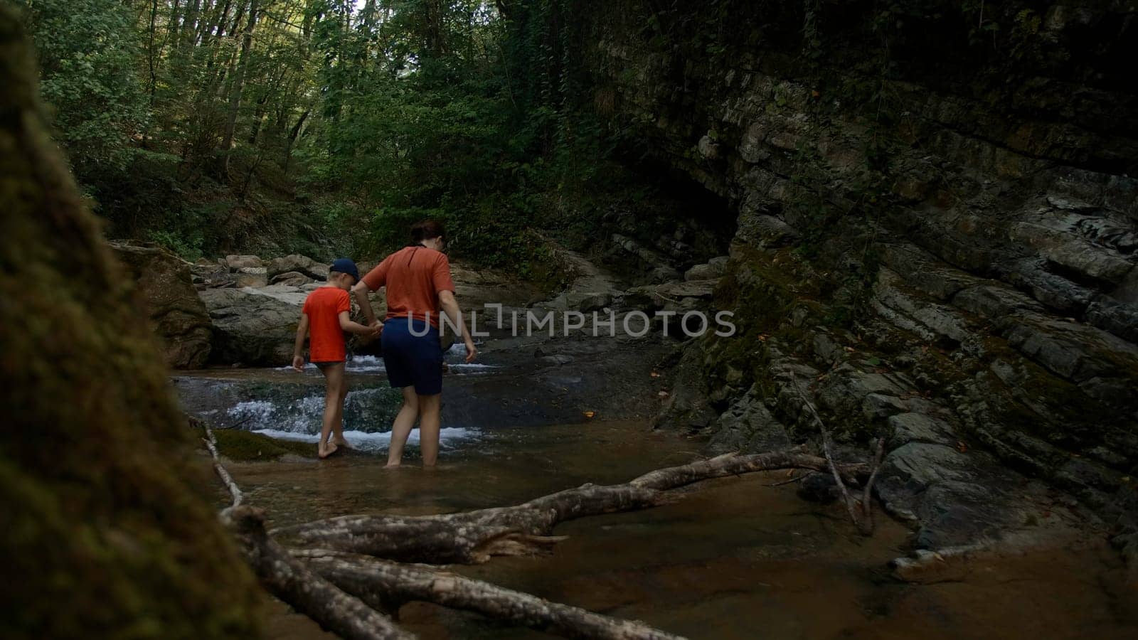 Boy and mother walking among rocks in cold stream. Creative. Hiking in wild nature. by Mediawhalestock