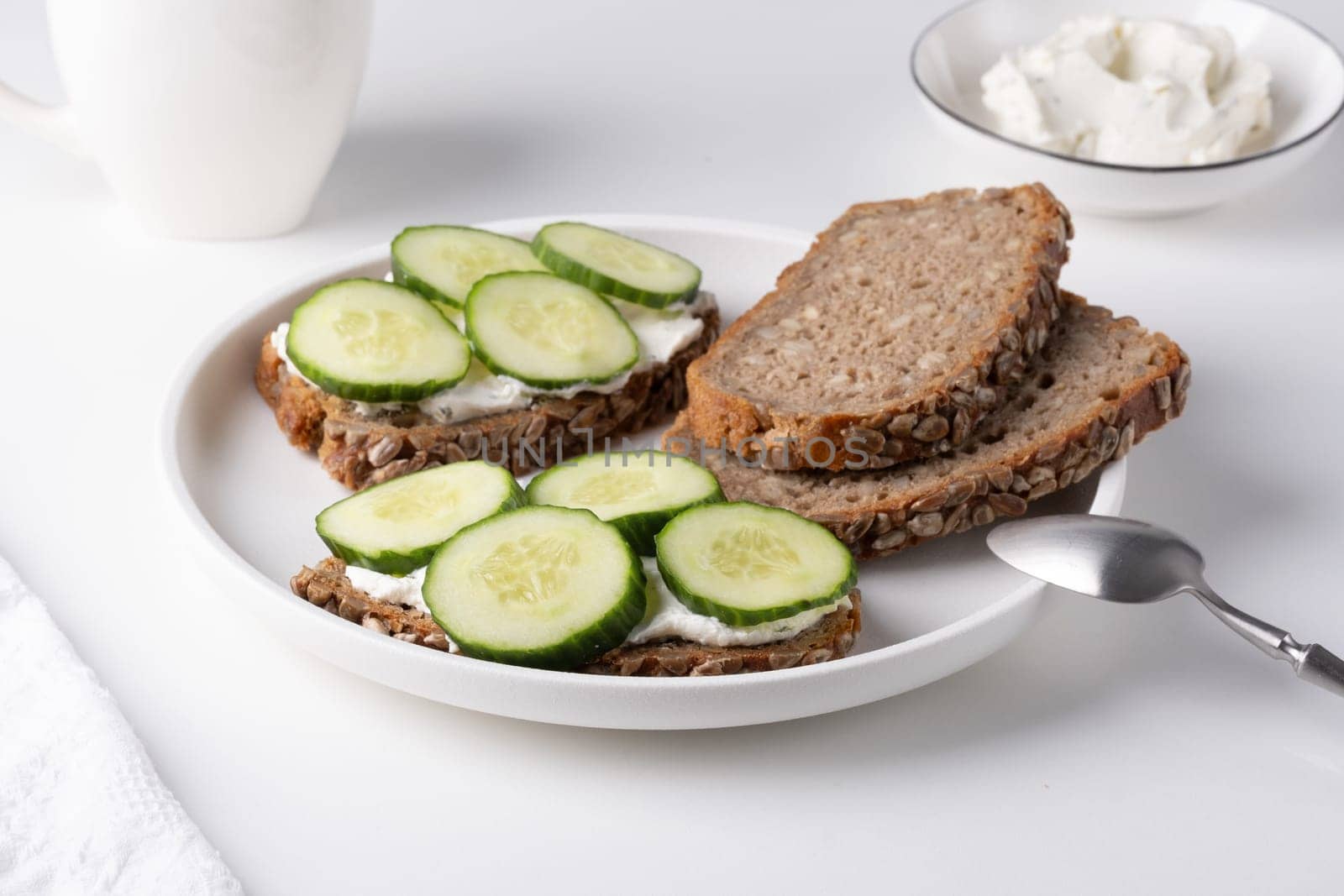 Rye bread with cream cheese and cucumbers on a white table. Whole grain rye bread with seeds.