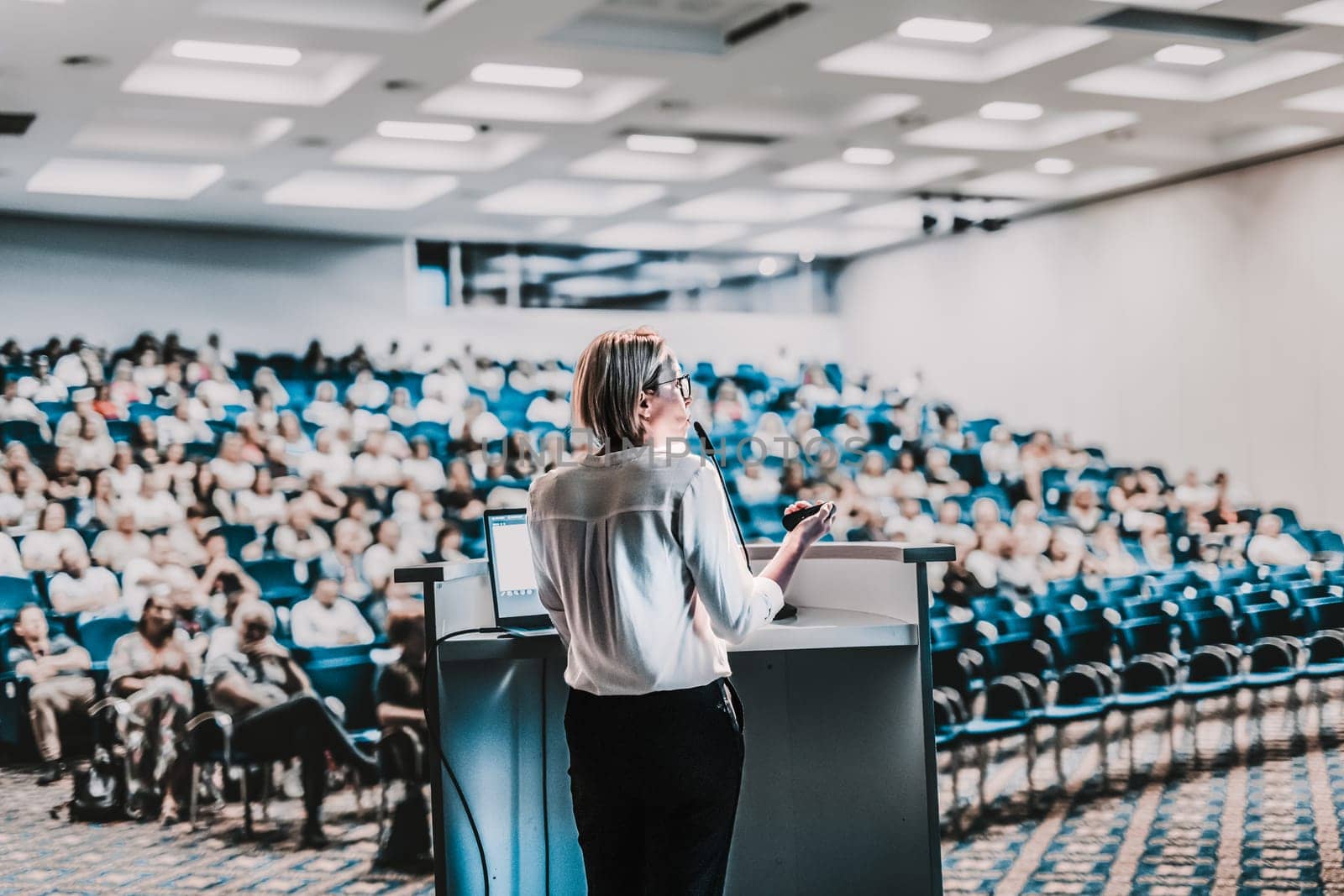 Female speaker giving a talk on corporate business conference. Unrecognizable people in audience at conference hall. Business and Entrepreneurship event. by kasto