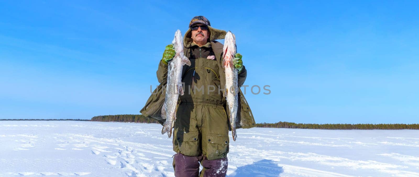 Man Holding a Fish pike in the Snow. Winter fishing, adventure. Banner, copy space