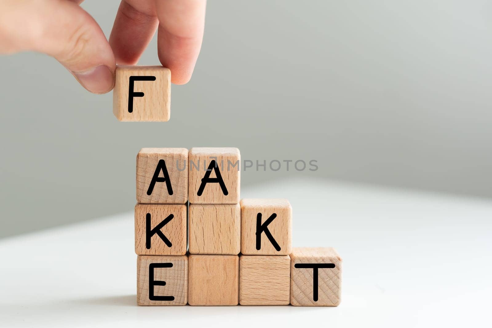 A man in a blue shirt composes the word FAKE from wooden cubes vertically. High quality photo