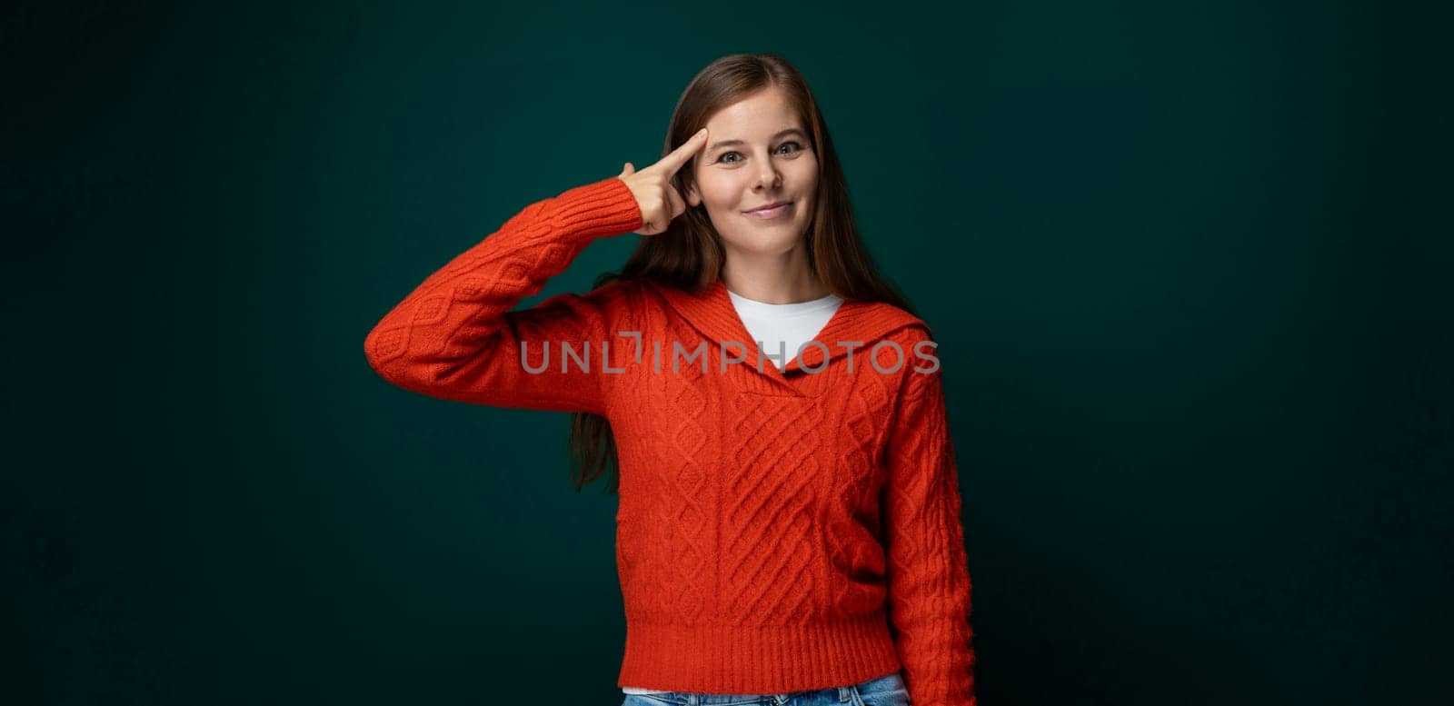 Attractive young woman dressed in a red sweater smiling on a green background by TRMK