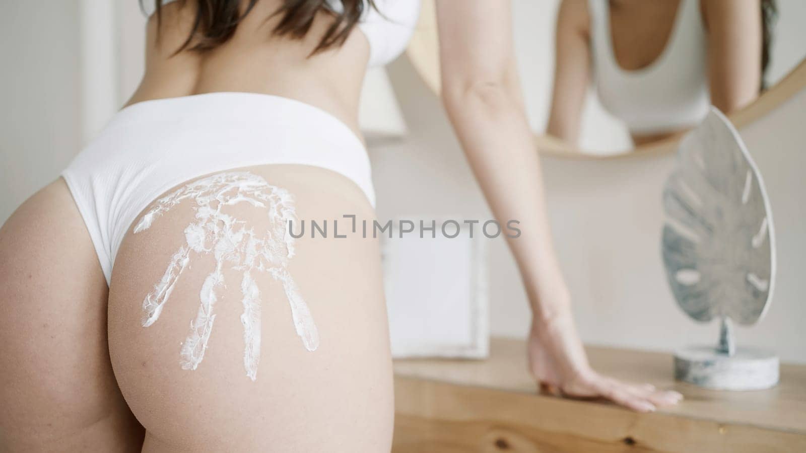 Women 's rest . Action . A beautiful young woman model in underwear who puts white cream on her body and poses next to a mirror. High quality 4k footage