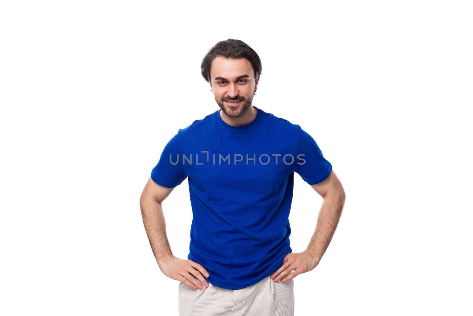 young well-groomed brunette man with a beard dressed in a blue T-shirt among a white background.