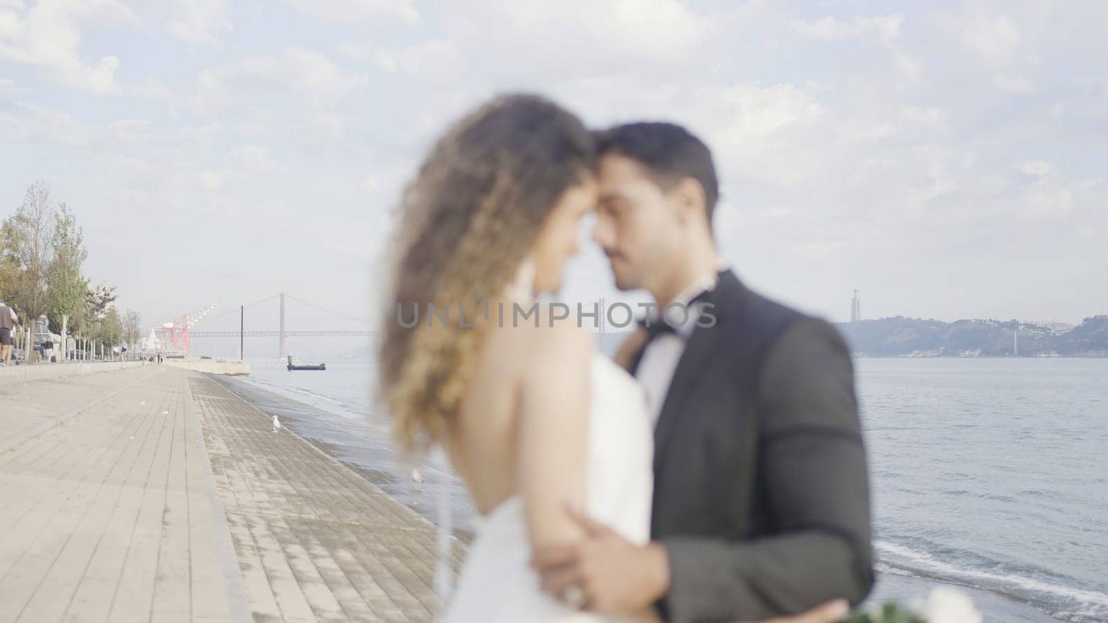 Beautiful couple in love hugs on embankment. Action. Elegant couple in suits during date on embankment. Beautiful couple of lovers tenderly embrace on embankment on sunny day.