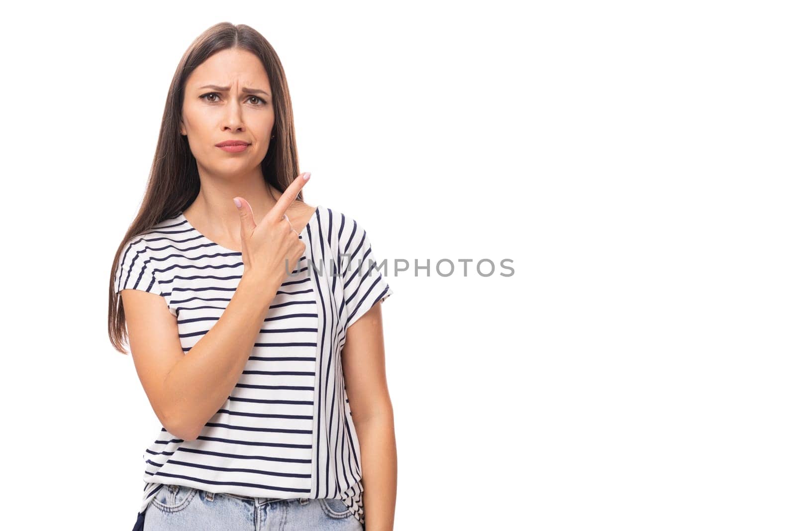 young positive pretty european brunette woman in a striped t-shirt points her finger on a white background with copy space.