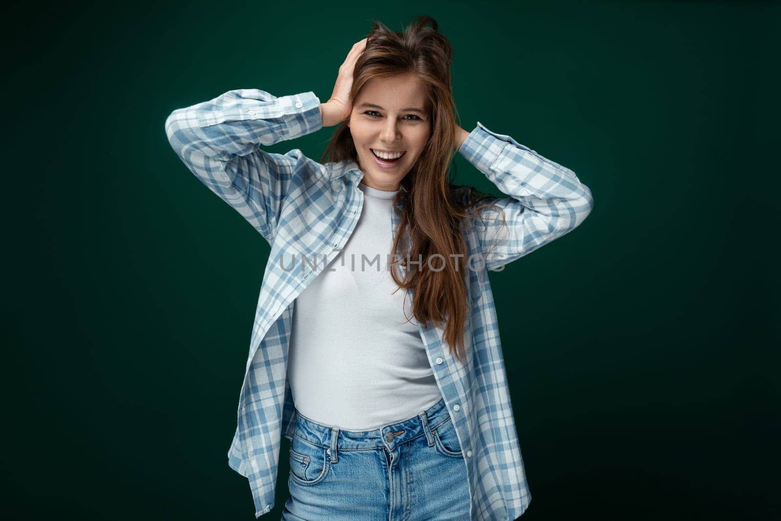 Positive European woman dressed in a stylish shirt and jeans on a green studio background by TRMK