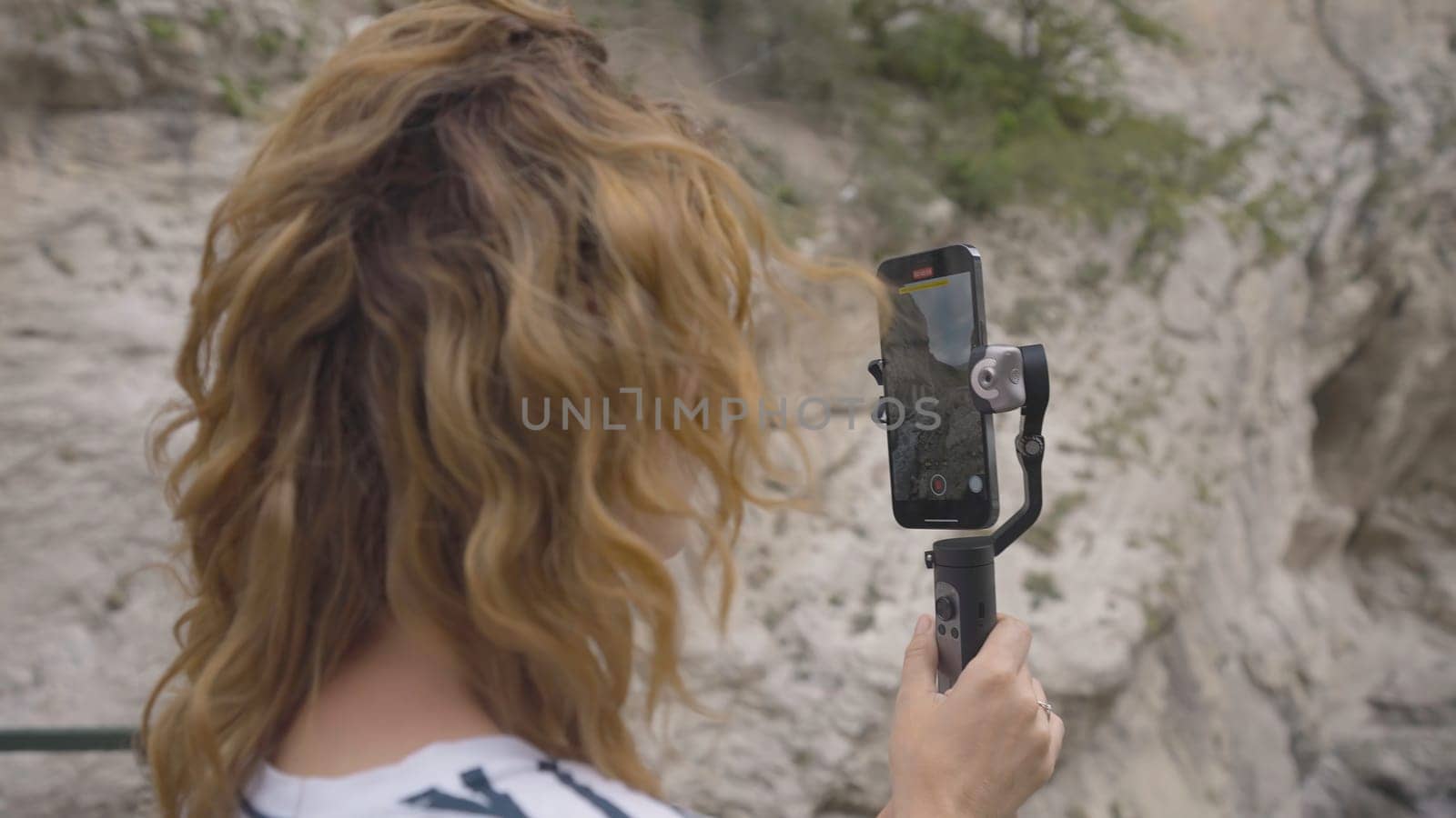 Beautiful woman takes pictures on phone with steadicam. Action. Young woman takes pictures on phone with manual stabilizer. Traveler takes pictures on hand-held steadicam in mountains.