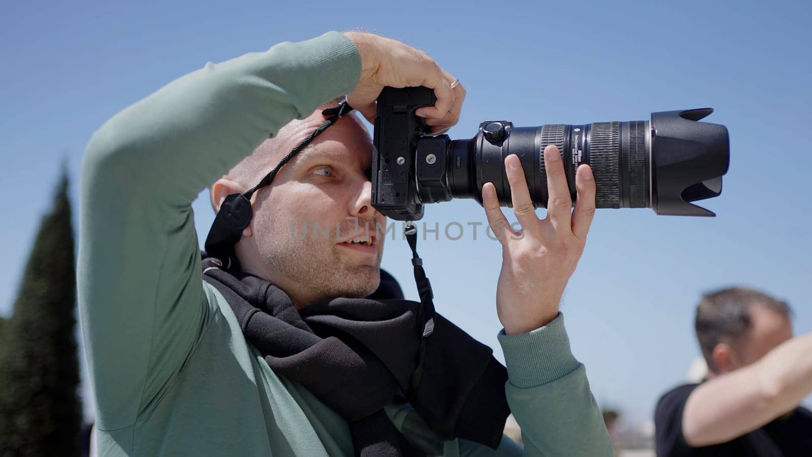 Side view of a male photographer with a professional camera outdoors. Action. Man holding camera and taking pictures