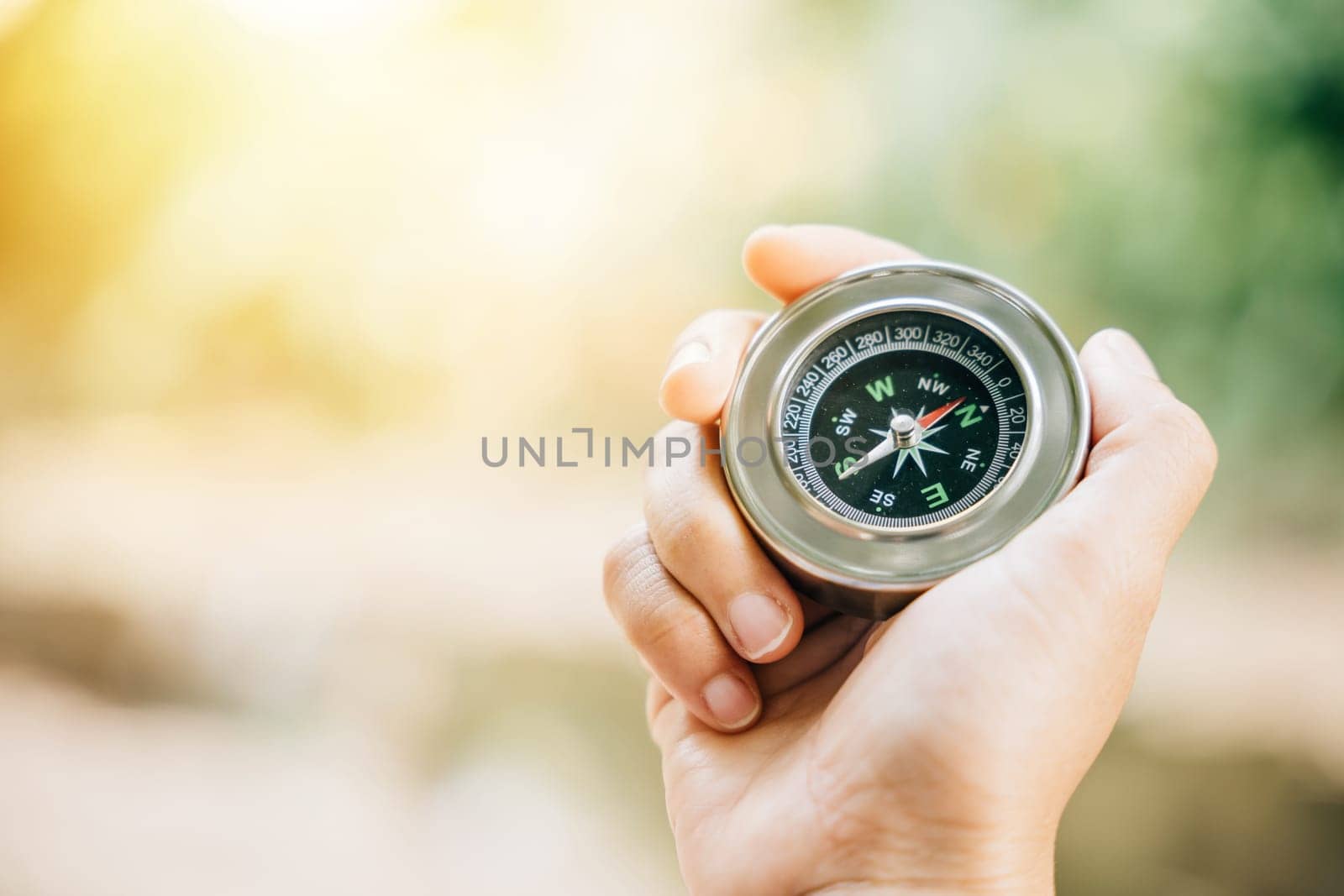 A traveler hand holds a compass in a park representing the quest for direction and guidance. Amidst nature beauty the compass signifies exploration and discovery.