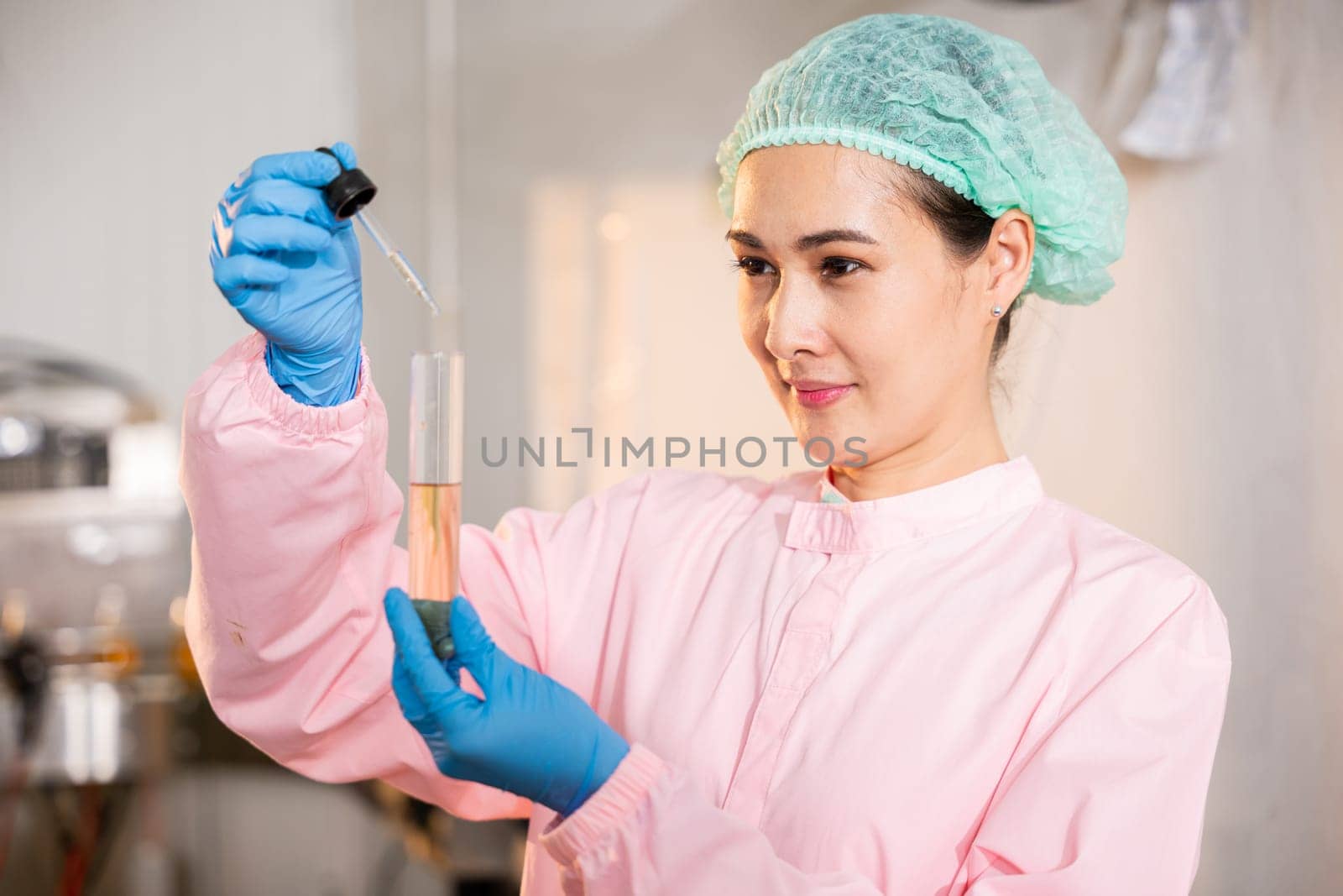 In juice beverage factory woman food engineer showcases food and beverage quality and safety testing concepts by utilizing test tubes for sampling basil or chia seeds in bottled products.