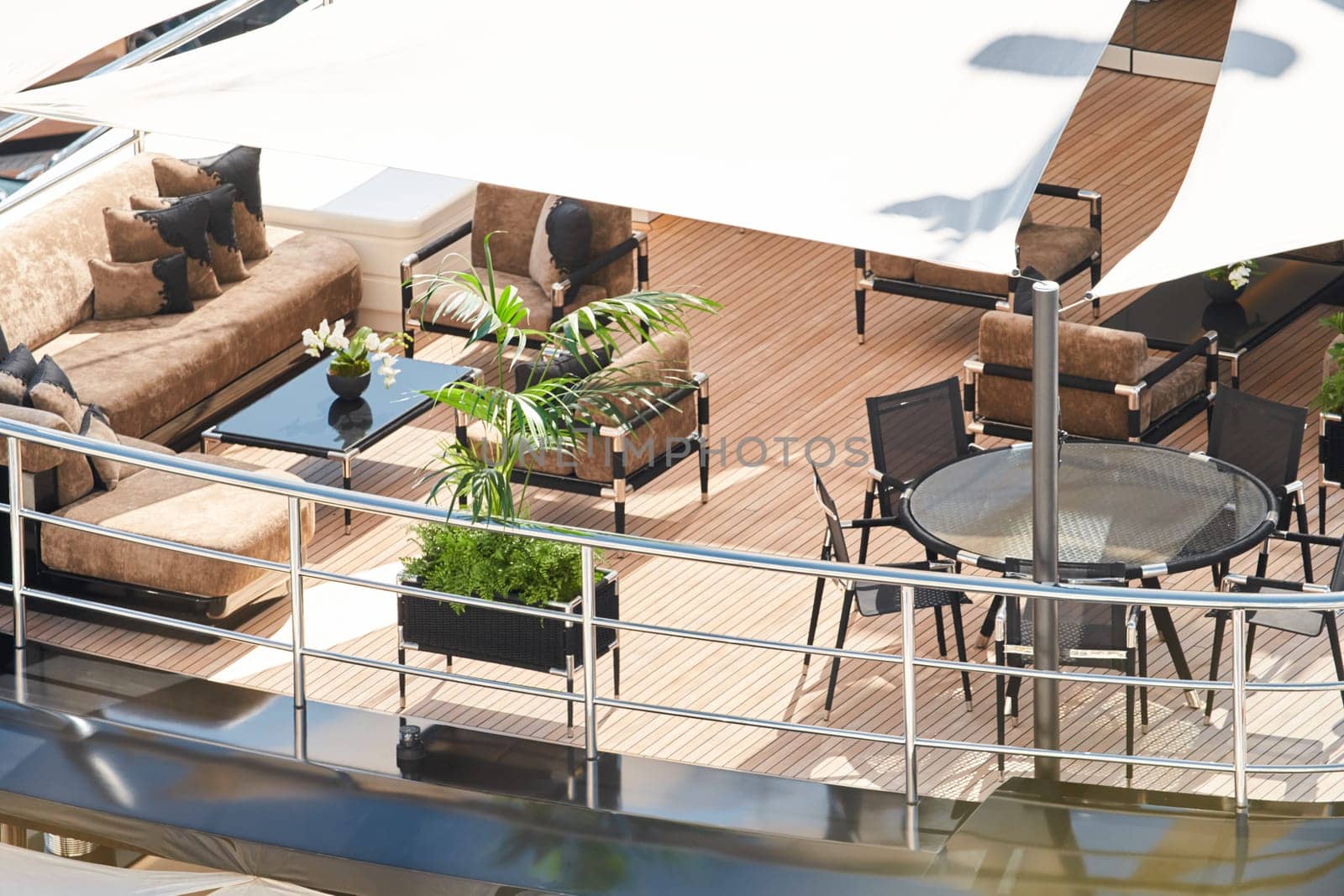 Close up footage of a relaxation area on the open teak deck of an expensive megayacht at sunny day, with awnings stretched over the deck to protect from the sun, wealth life, table and chairs. High quality photo