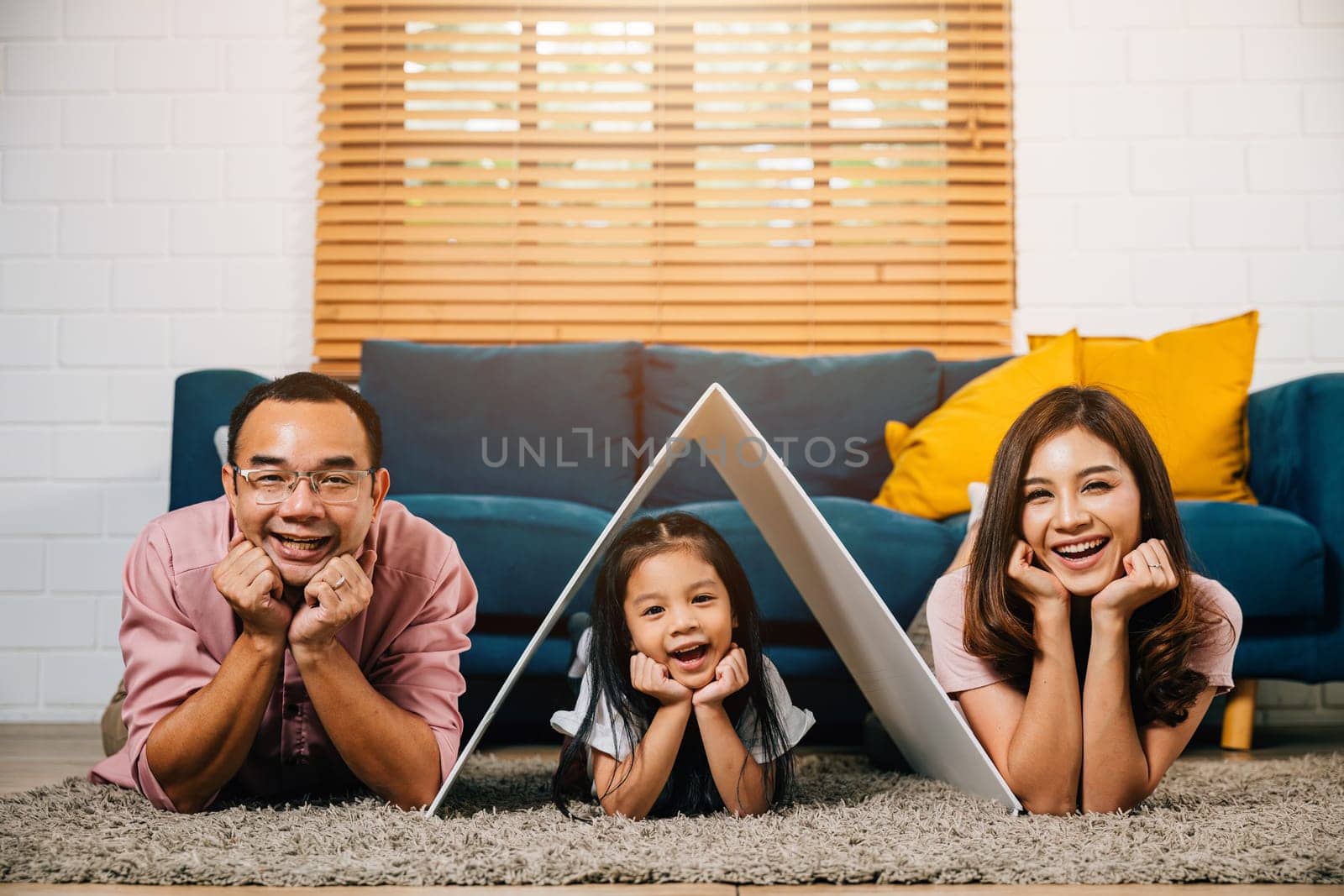 In their new house a loving family on a couch holds a cardboard roof showcasing the essence of happiness and security. Asian parents and their daughter are the picture of affectionate togetherness.