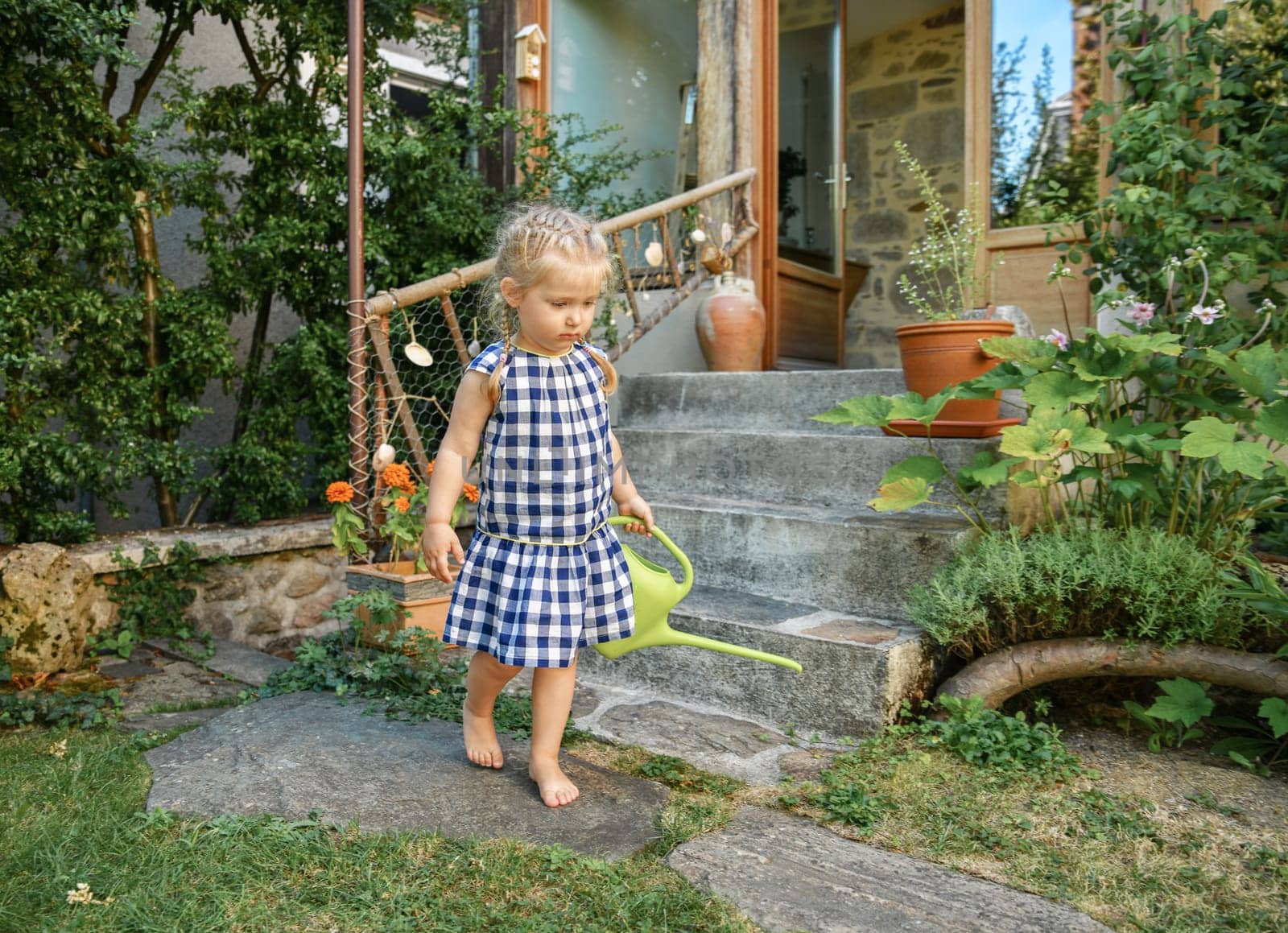 Little girl in a garden with green watering pot