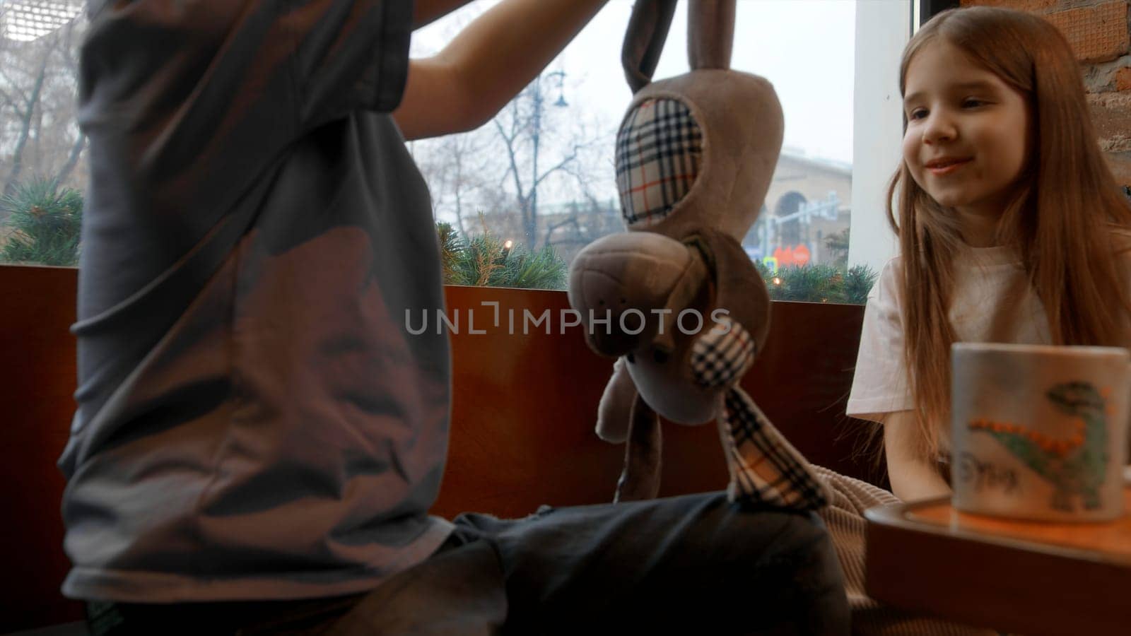 Kids playing with a dog toy at a table cafe. Stock footage. Children having fun and holding a puppy toy