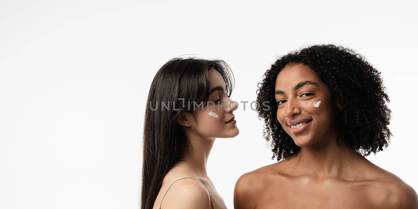 Female models of various ages celebrating their natural bodies in a studio. Two confident and joyful women smiling radiantly, having used cosmetics.
