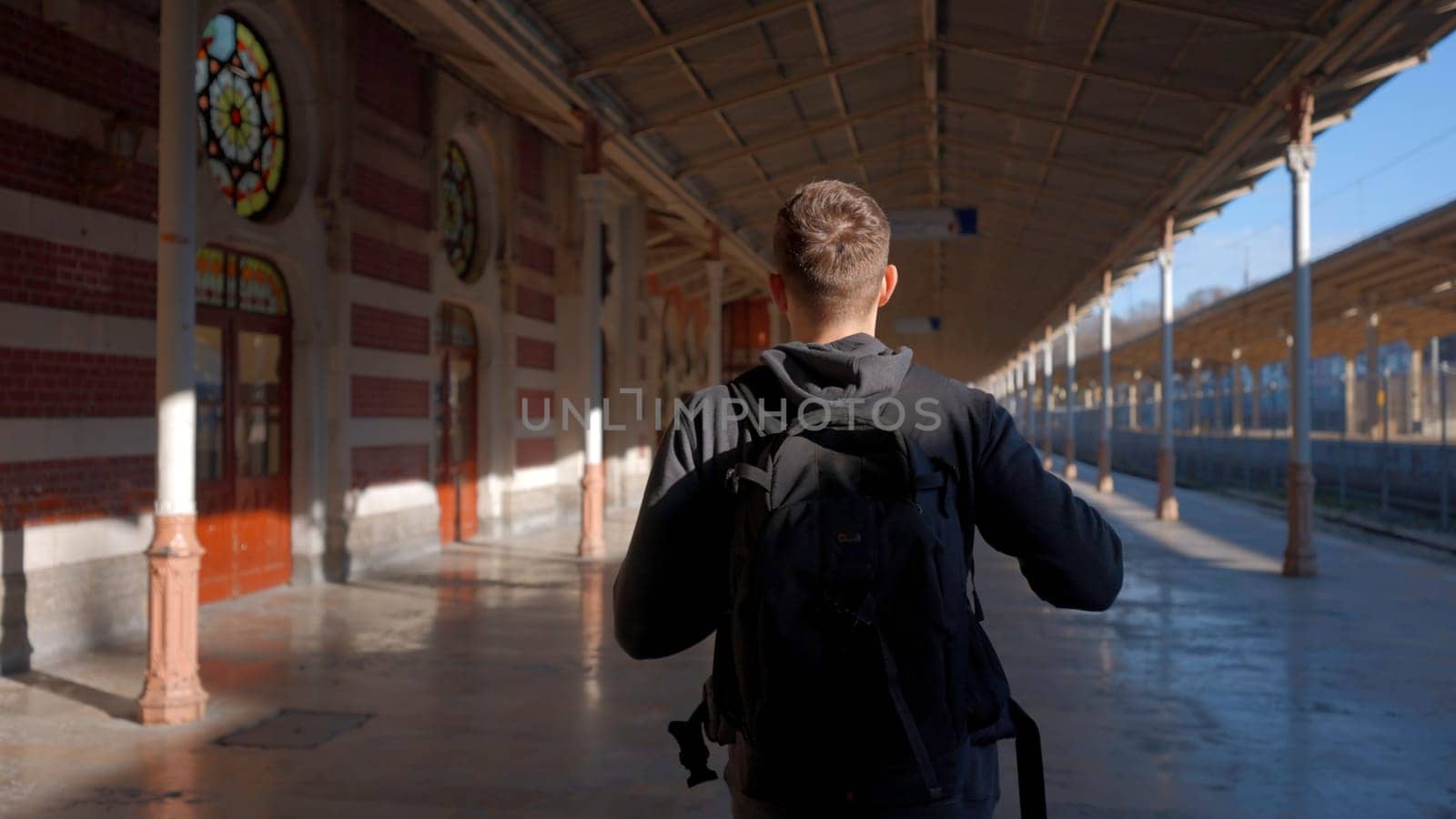 Young man with backpack walking along empty railway station. Action. Travel concept