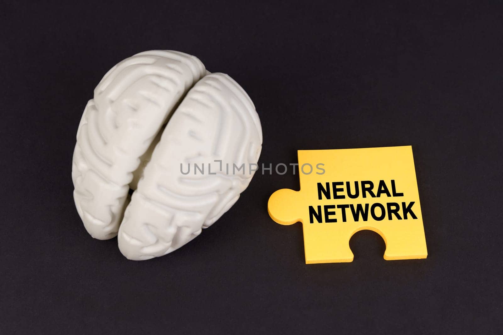 On a black surface lies a brain and a yellow puzzle with the inscription - Neural Network. Education and technology concept.