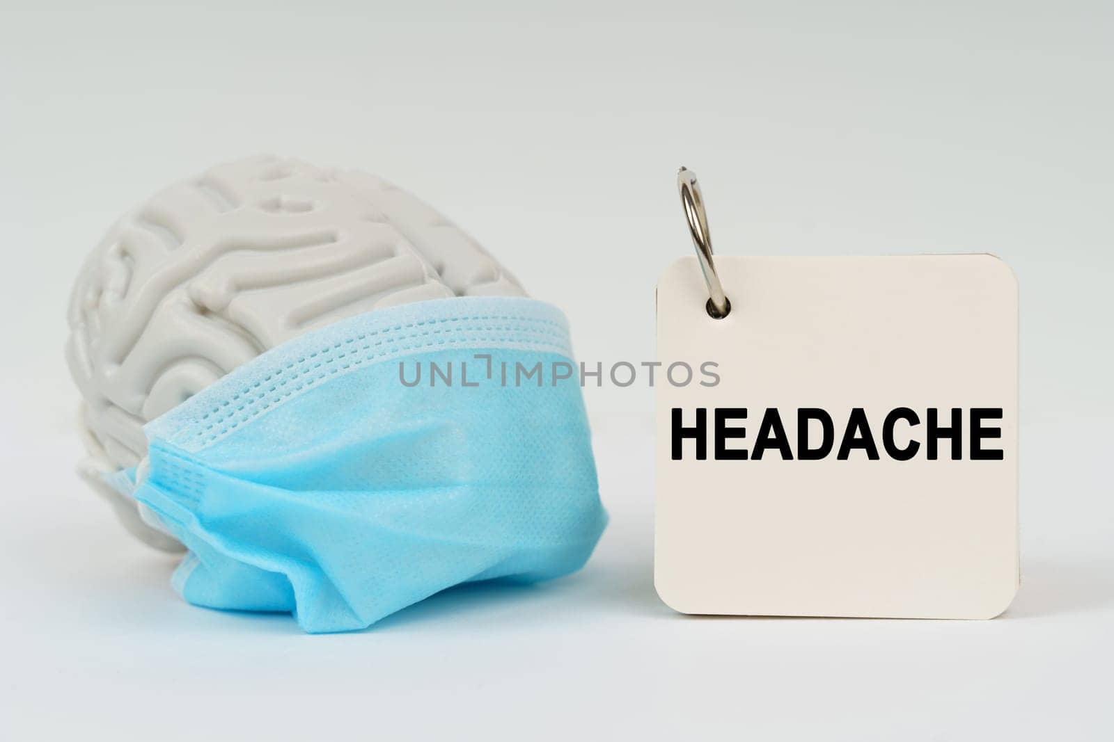 Medical concept. On a white surface there is a brain with a blue mask and a notepad with the inscription - Headache