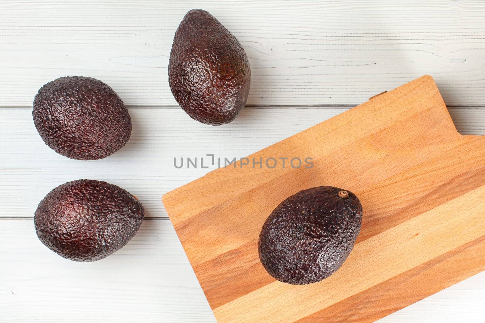 Whole avocados (dark brown bilse variety) on white table, with cutting board next by Ivanko