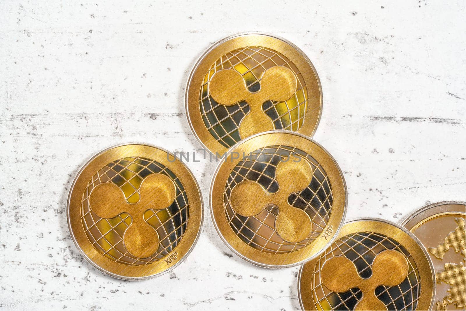 Tabletop photo - detail of golden ripple cryptocurrency coins scattered on white board by Ivanko