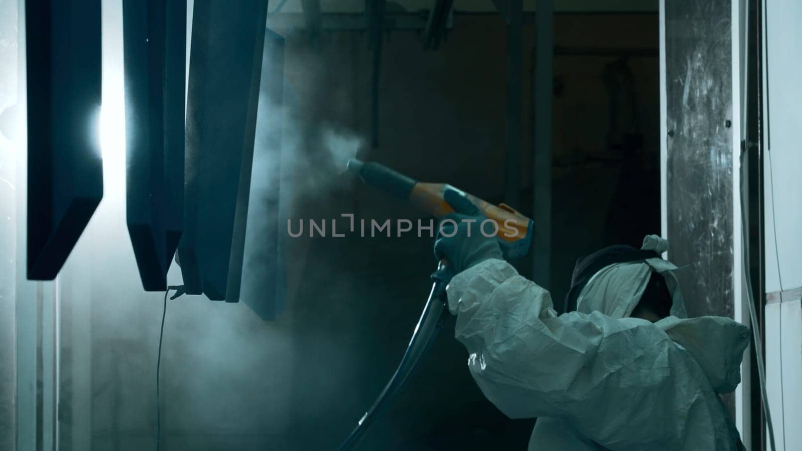 Worker with a spray gun painting parts in metal workshop. Creative. Powder coating of metal products
