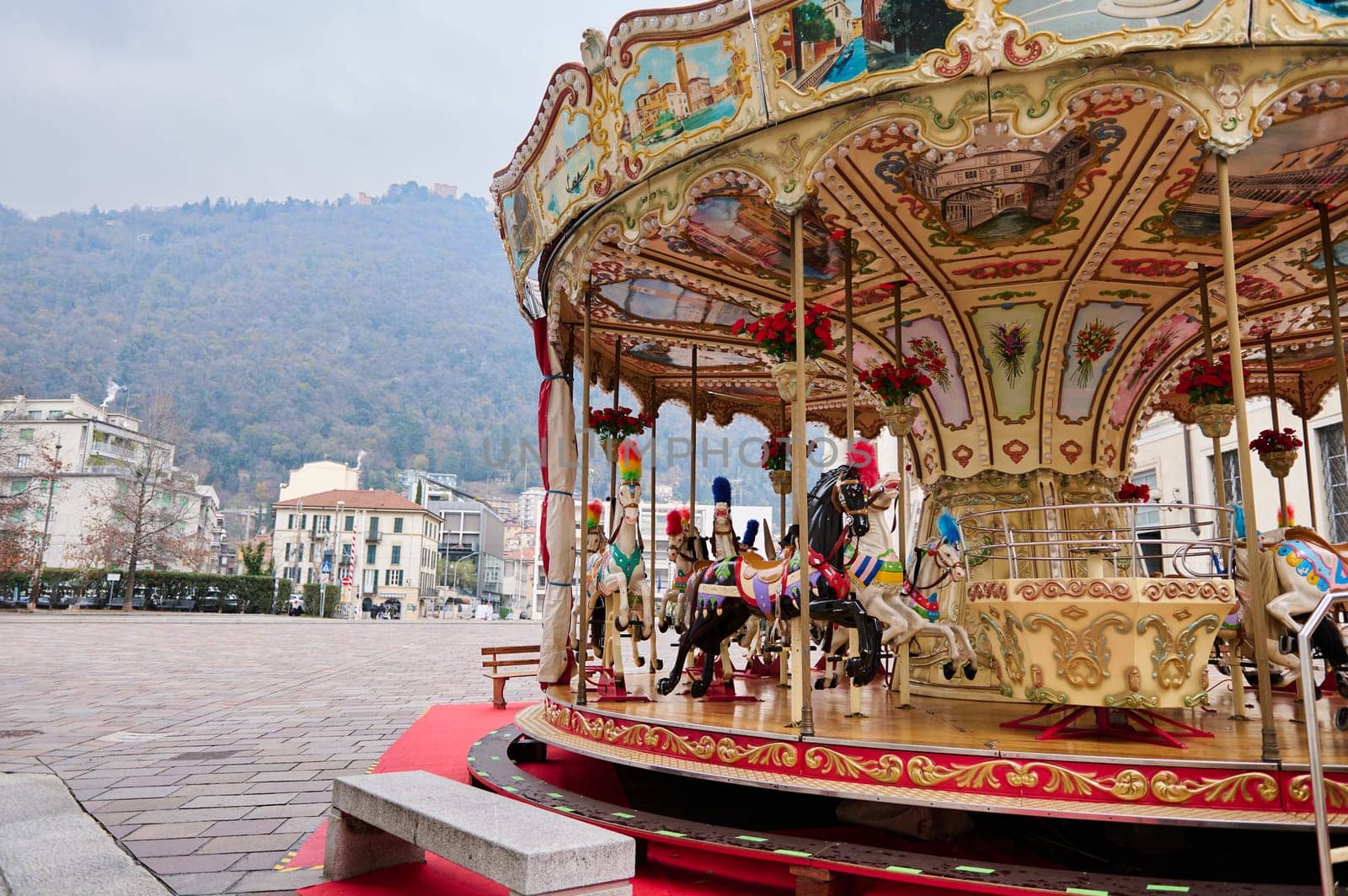 A merry go round, Victorian carousel at Christmas fairground in Como, against Italian Alps backdrop on cloudy winter day by artgf