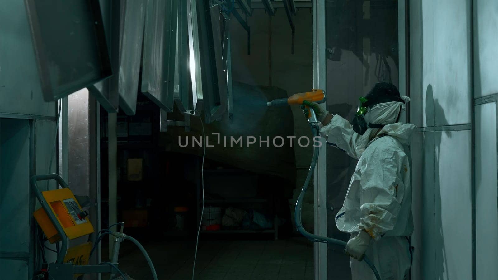 Process of powder coating of metal parts at a steel factory. Creative. Worker in protective suit with paint gun