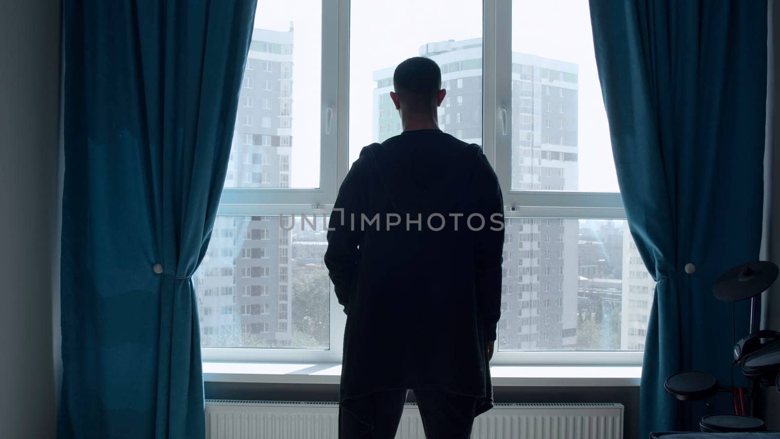 An adult man standing in the room. Media. A beautiful slender silhouette of a man who stands in a bright room with a large window and looks into the distance. High quality 4k footage