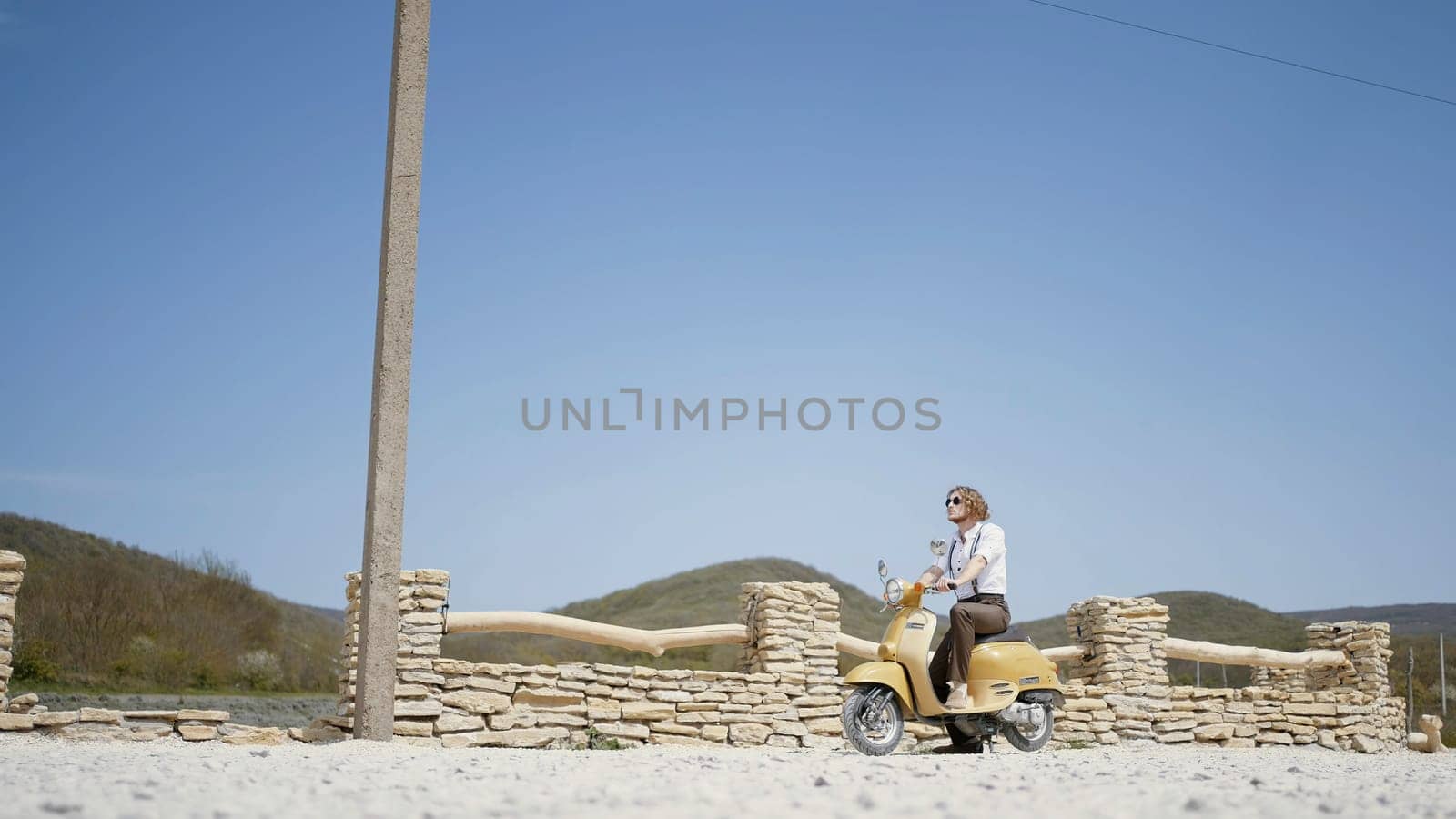 Summer landscape with a man. Action. A handsome man with long hair on a small green motorcycle on a beautiful landscape with blue sky and mountains
