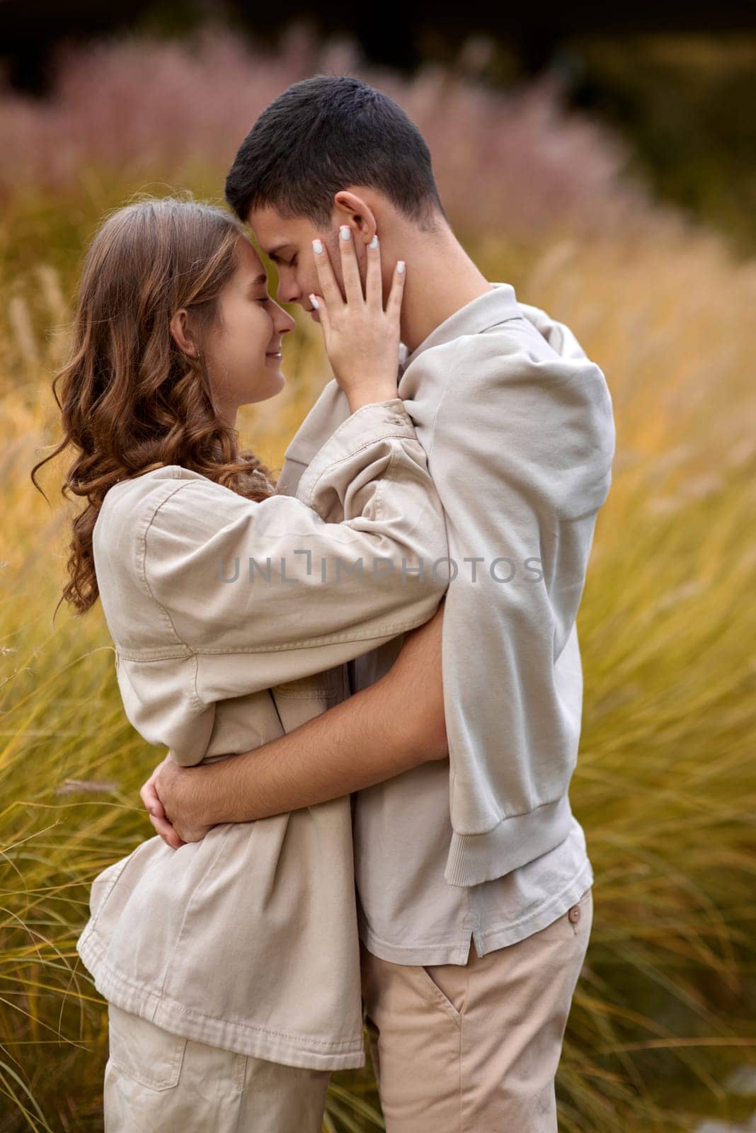 Happy couple on autumn walk outdoors. Two lovers in autumn park. Love and tender touch. Gentle hugs. Young man and woman in classic autumn colors outfit on a romantic date in a cozy park. Young girl and guy with blond hair kisses, show love, affection. Boy and girl of European appearance with warm clothes, pictures with soft background bokeh blur fall. Concept of happiness, joy by Andrii_Ko