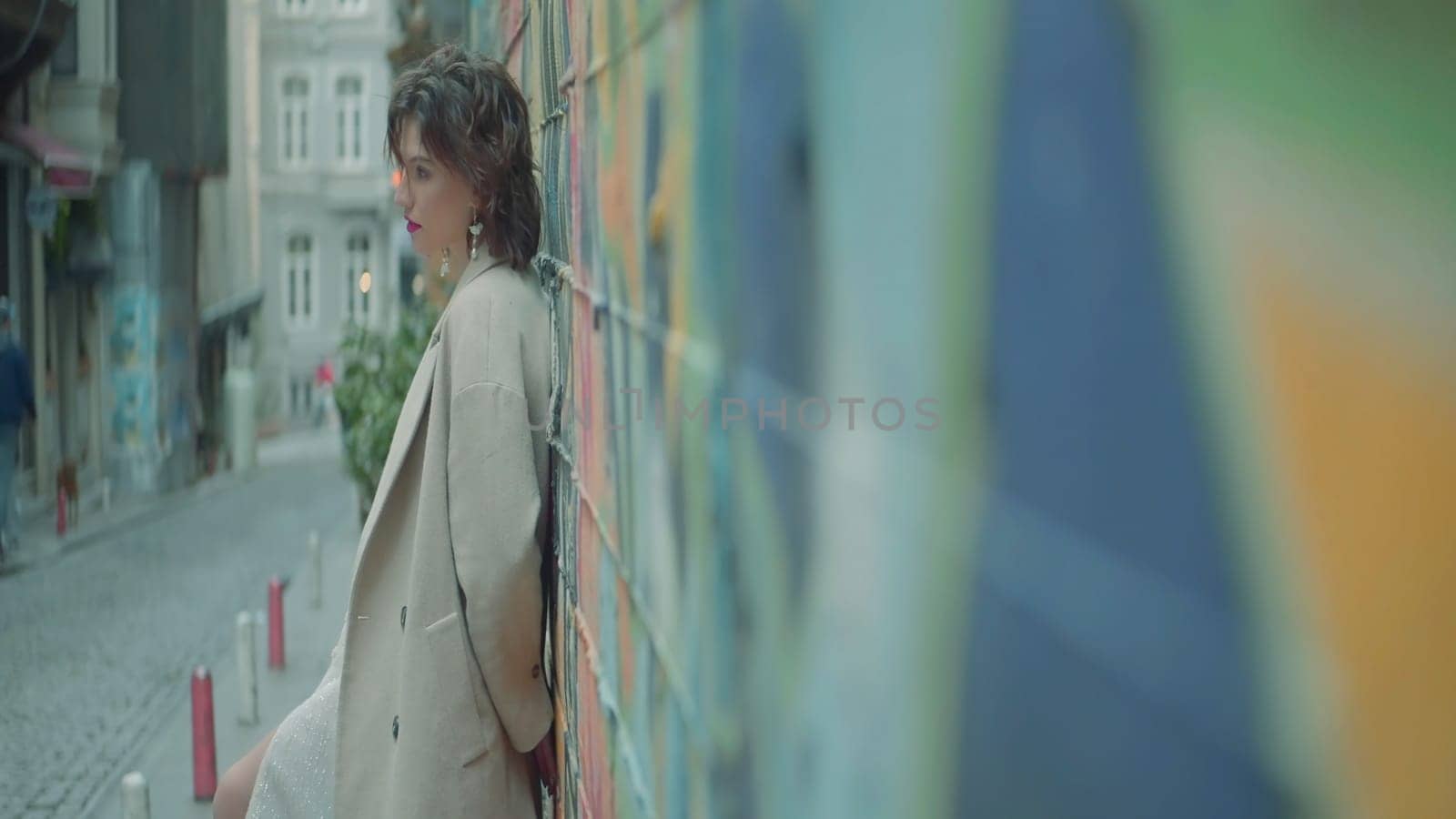 Stylish young woman stands at street wall. Action. Side view of attractive young woman against wall. Woman is standing on street by wall.