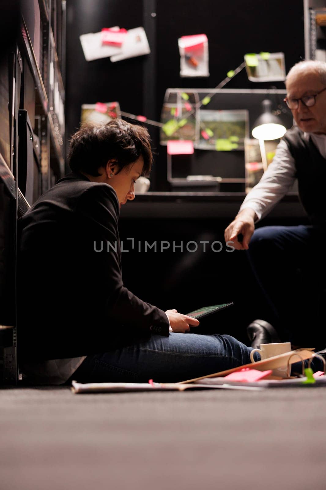 Tired police officer analyzing victim report in arhive room by DCStudio