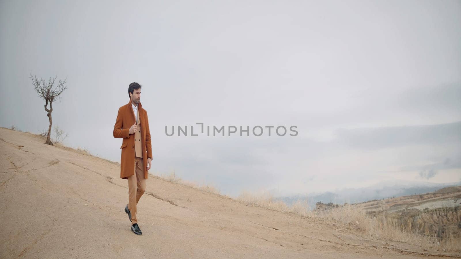 Elegant man walks on sand. Action. Stylish man in suit walks through sandy landscape. Stylish man walks on sand as if in advertisement.