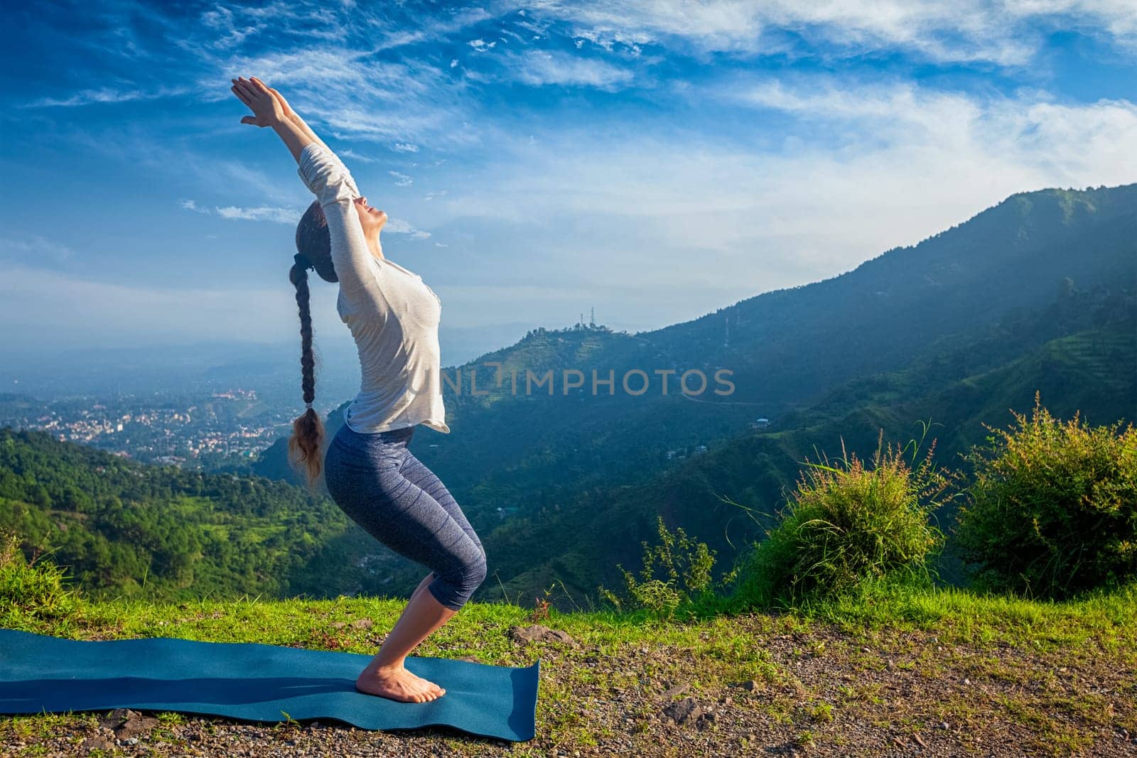Young woman doing yoga asana Utkatasana (chair pose) outdoors in mountains Himalayas in the morning. Himachal Pradesh, India