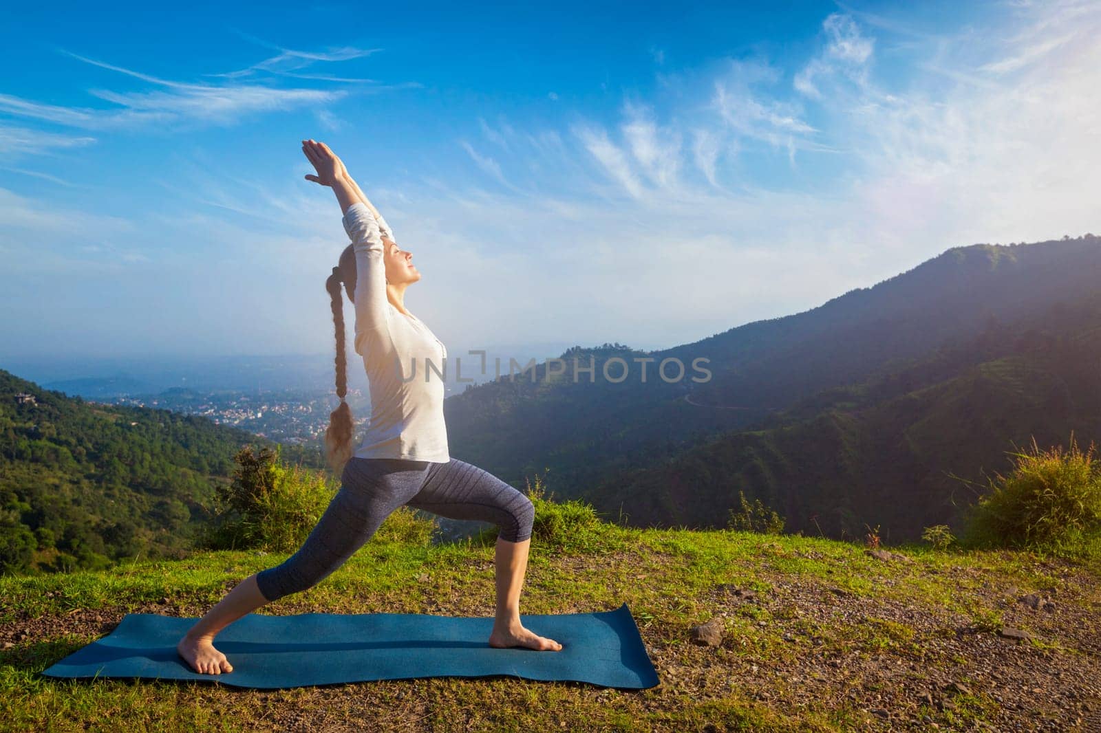 Yoga outdoors - woman doing yoga asana Virabhadrasana 1 - Warrior pose posture outdoors in Himalayas mountains in the morning