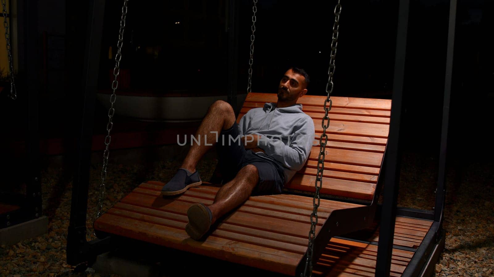 Man lying on wooden bench and swinging slowly, looking thoughtful. Media. Man thinking about life on woden bench
