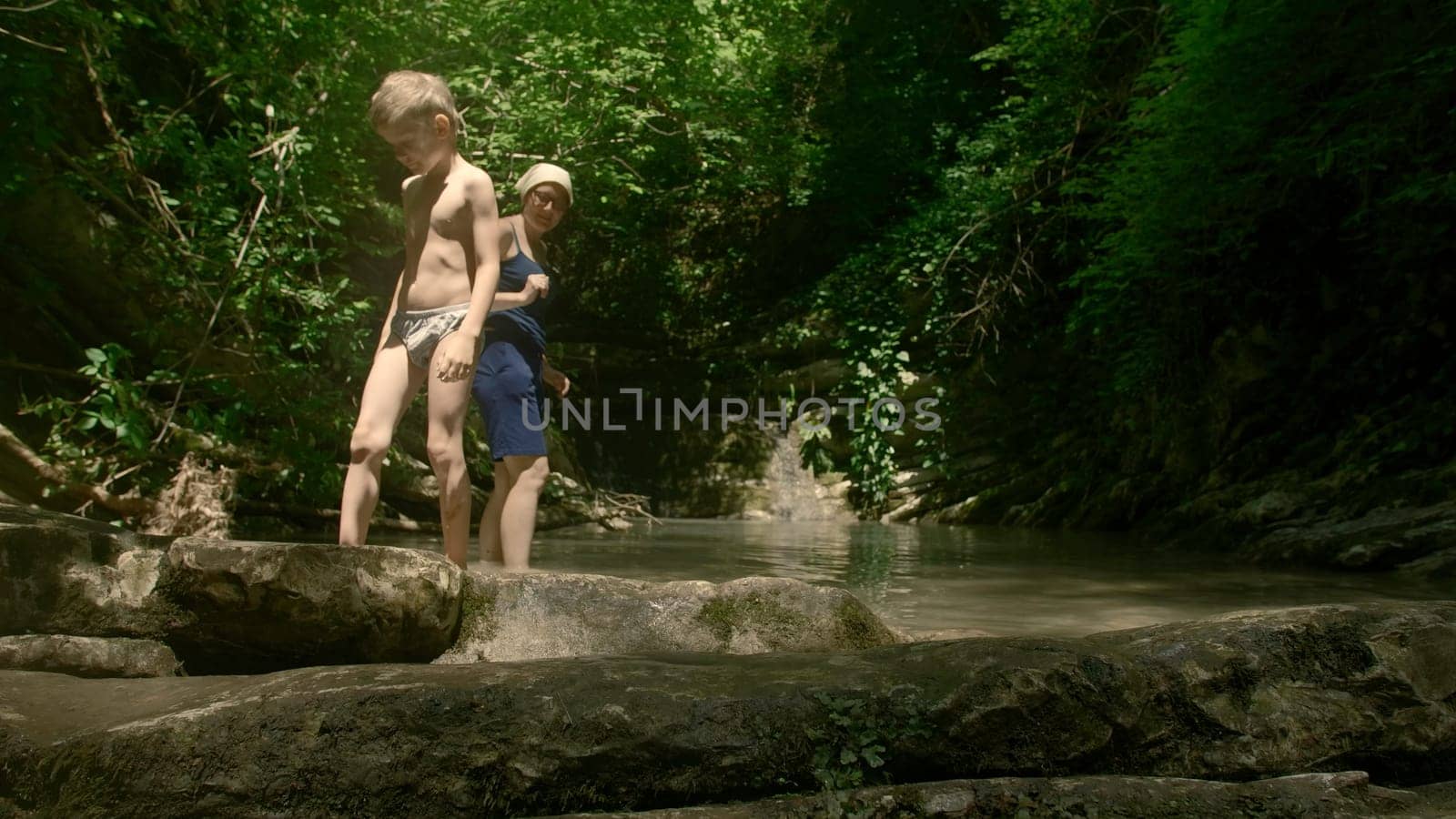 Boy kid and his mother having a great time in the cold mountain stream. Creative. Beautiful river and jungles