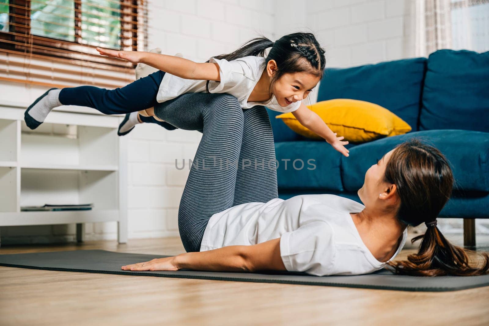 A harmonious family practices the little bird posture in yoga at home by Sorapop