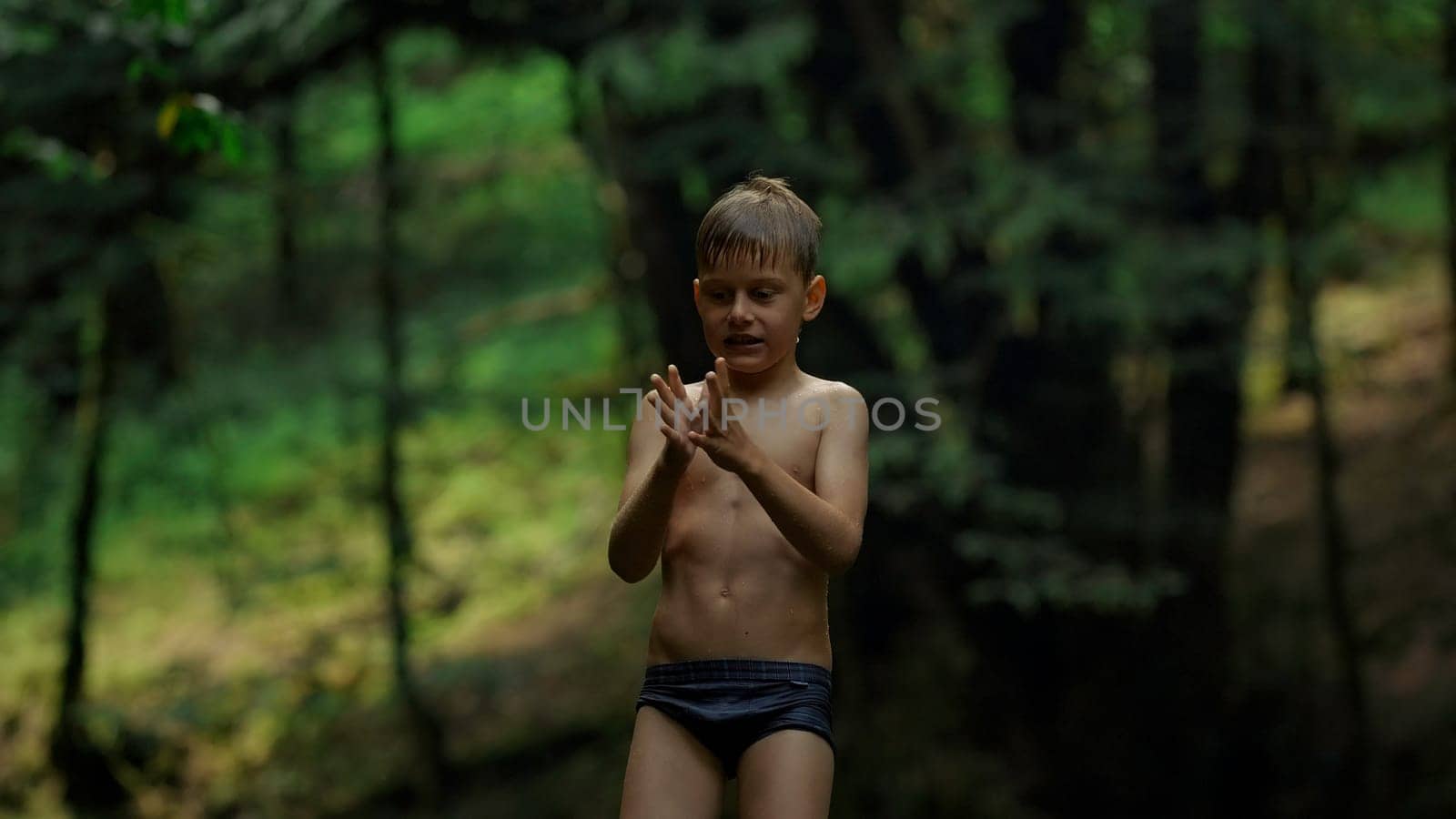 Caucasian boy Mowgli enjoys nature, wet after swimming. Creative. Boy child in swimwear with green jungles on the background