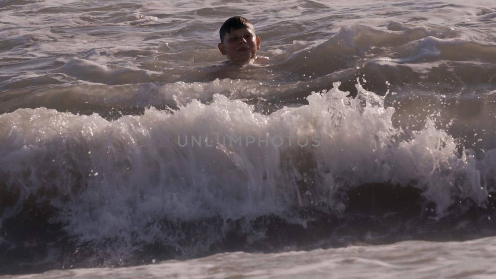 Bathing season. Creative. The boy swims in the sea, which waves under the bright rays of the sun. High quality 4k footage