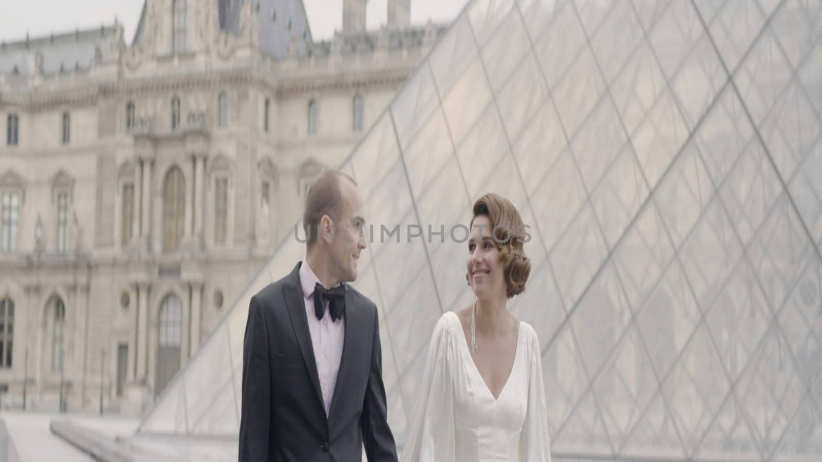 Walking bride and groom with a glass facade Louvre pyramid. Action. Loving beautiful man in woman on their wedding day