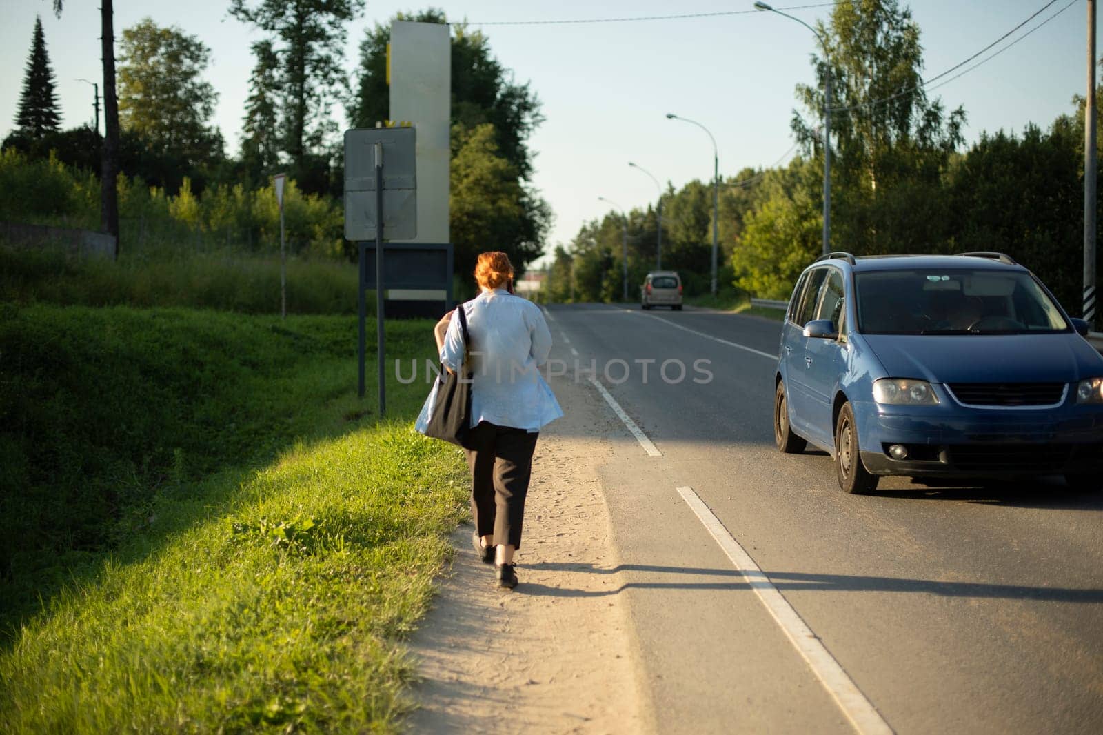 Girl walks on side of road. Walking in summer on foot. Man on track. Late for bus. Highway side.