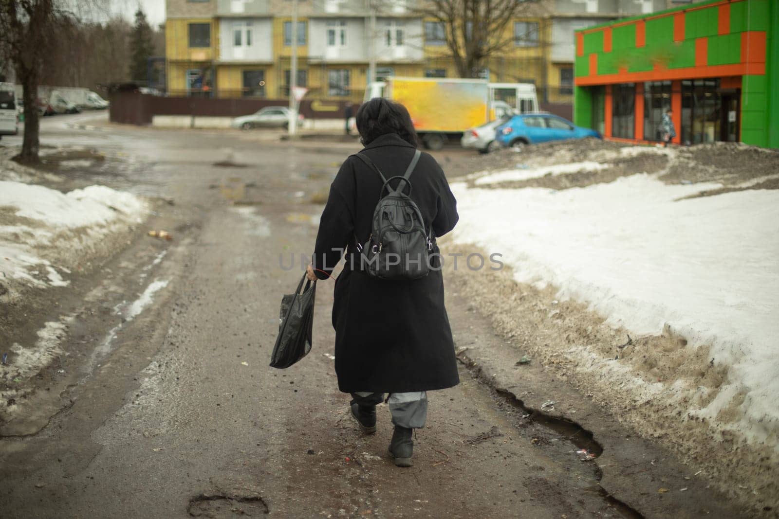 Woman walks along dirt road in city. Man in black jacket with backpack. by OlegKopyov