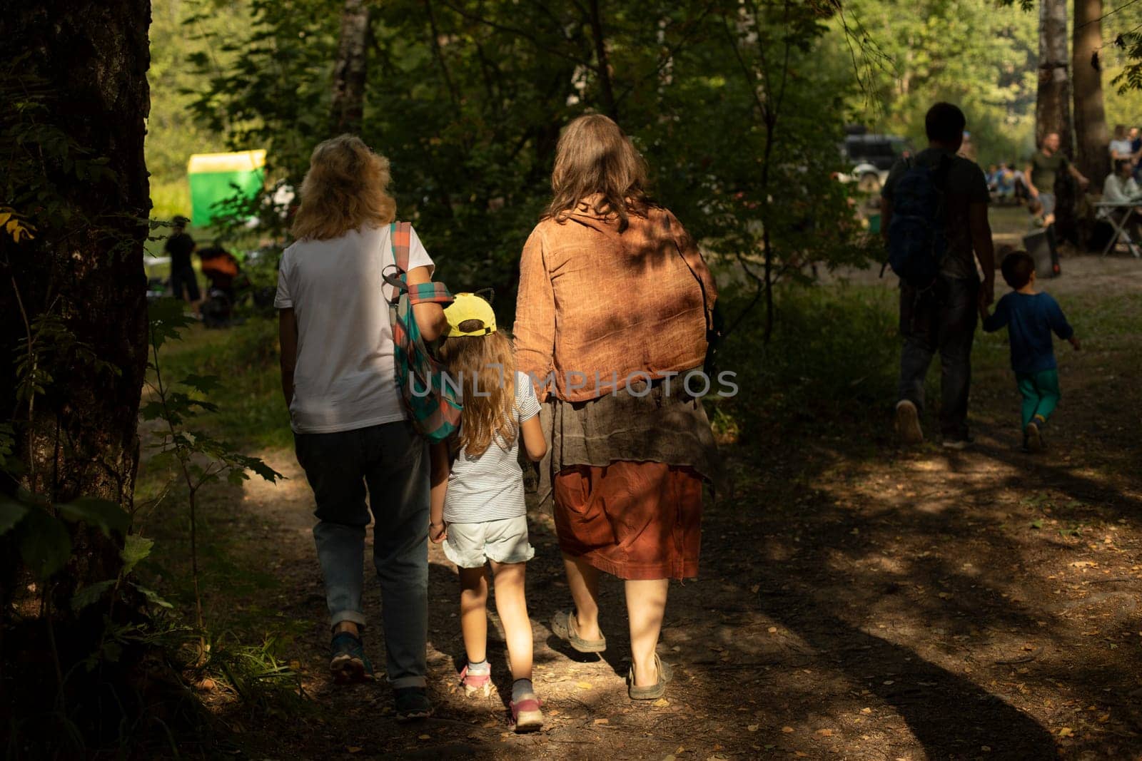 Family with child at festival in summer. Parents with child in park. Rest and travel. People from behind in sunlight.