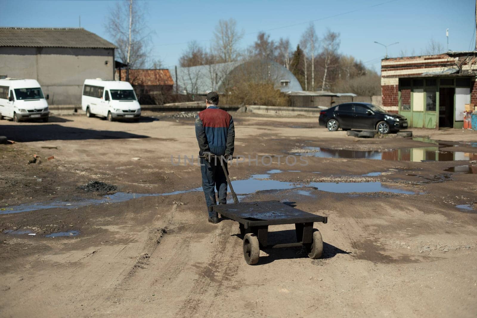 Man pulls cart down road. Worker is transporting empty forklift. by OlegKopyov